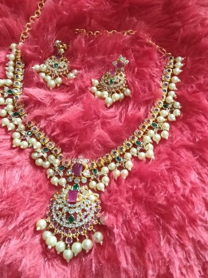 గులాబీ మరియు తెలుపు రాళ్లతో బంగారు పూత పూసిన చోకర్ నీలమణి, బహుశా చెవి రింగులతో సముద్రపు ఆకుపచ్చ పూసలు కూడా ఉండవచ్చు. యొక్క చిత్రం