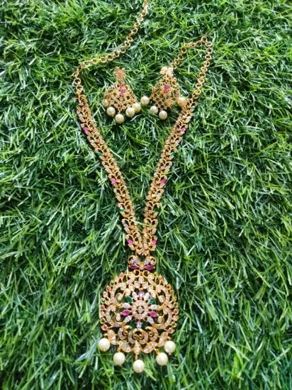 చెవి రింగులతో ఎర్రటి రాళ్ల గొలుసుతో నెమలి లేదా పూల డిజైన్. యొక్క చిత్రం